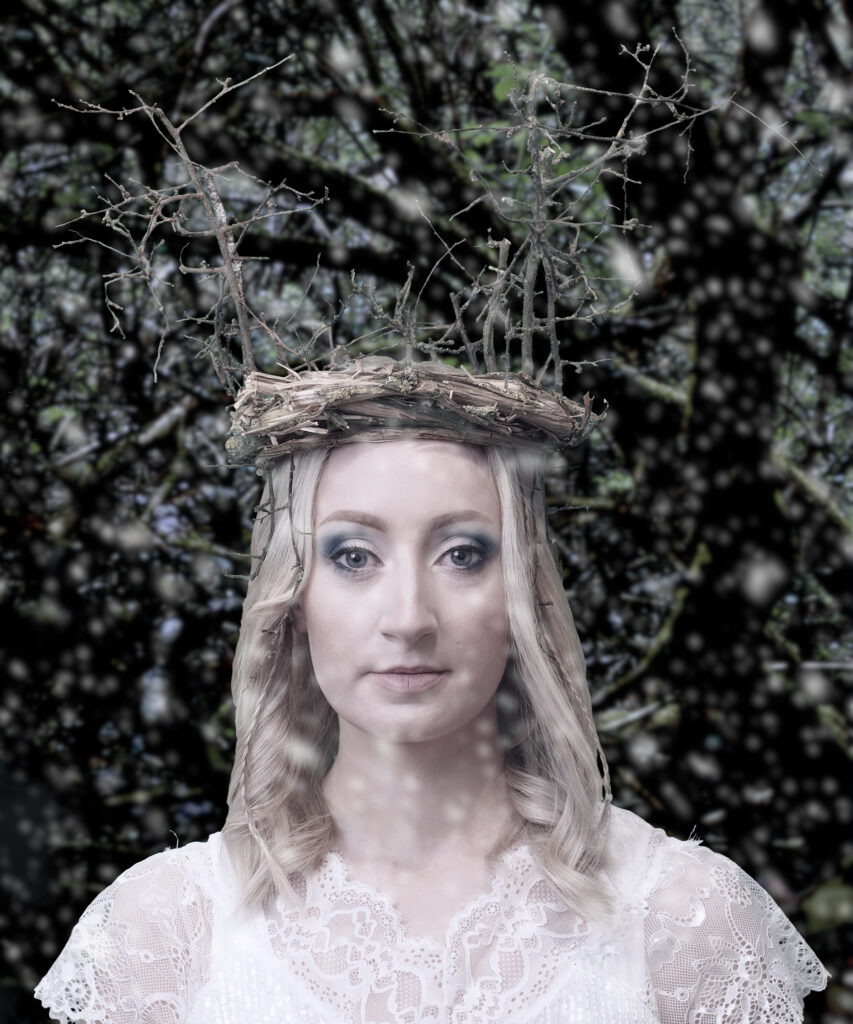 Creative portrait of a young woman with a crown of twigs. Wintery background with falling snow.