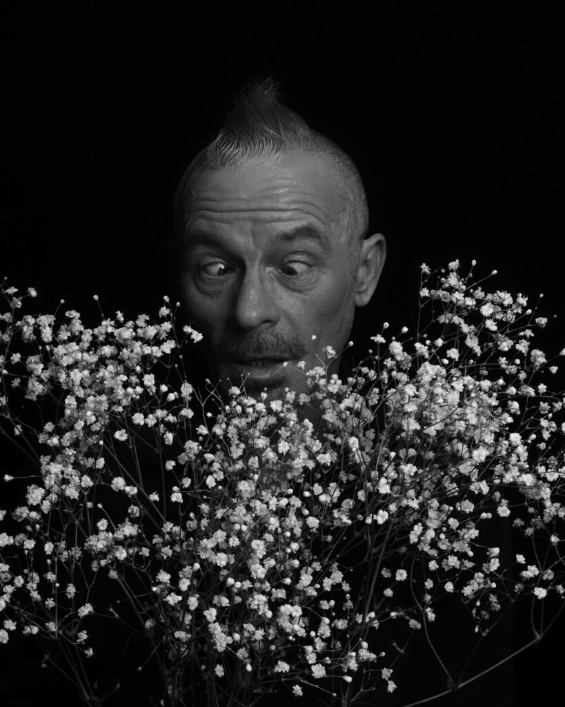 Portrait of a man. Monochrome. He's cross-eyed and peering down into a bunch of gypsophila flowers.