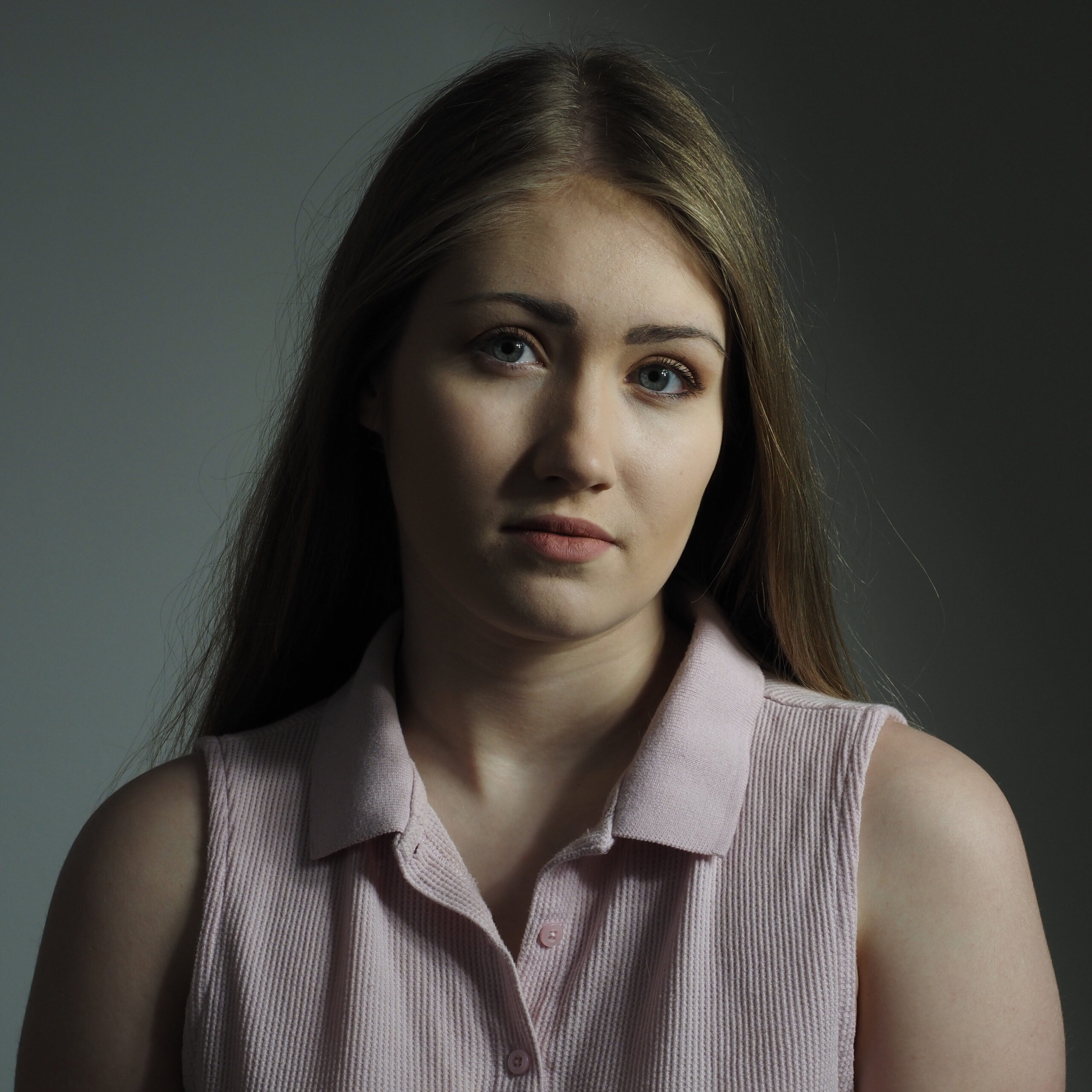 Portrait of a young woman, head tilted, looking serene. Partially lit background.